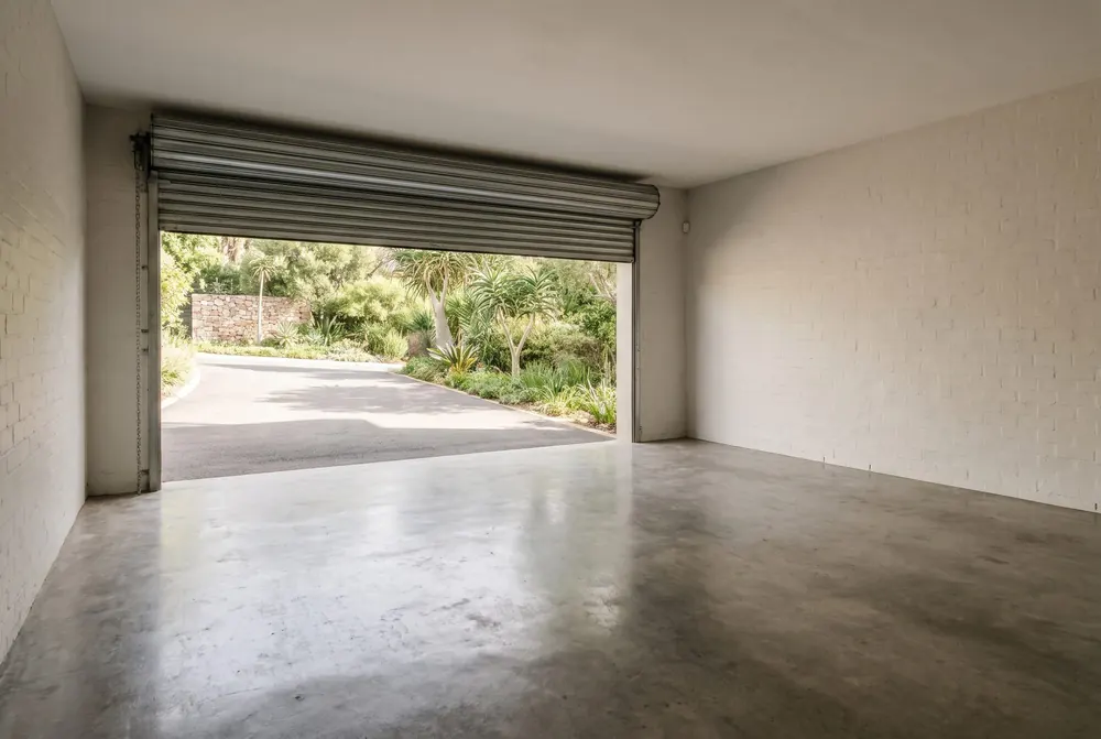 A double garage cleared to bare floor with the roller door open onto a sunlit driveway